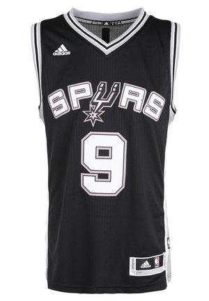 Man draagt een zwart San Antonio Spurs basketbalshirt met nummer 9 en zwarte Brooklyn Nets shorts, staand in witte sneakers.