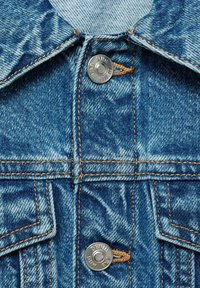 Denimjackenkragen mit blauen und hellblauen, abgenutzten Mustern. Verfügt über silberne Knopfdetails und kontrastierende orangefarbene Nähte.