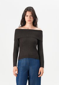 Dark brown ribbed off-the-shoulder sweater with long sleeves and fitted bodice. Paired with blue wide-leg jeans.