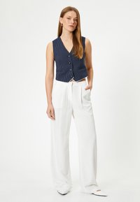Gilet à rayures navy avec boutons et décolleté en V, assorti à un pantalon large blanc. Tissu lisse, coupe ajustée et lignes épurées.