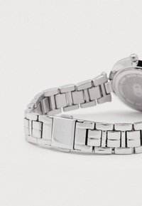 Ceas argintiu din metal cu design de bratara legata, avand o inchizatoare, carcasa rotunda si un finisaj neted si lustruit.