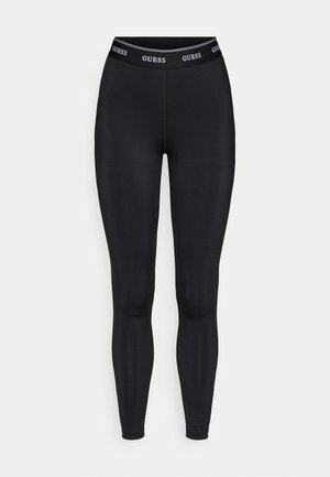Leggings nere in tessuto elasticizzato con una fascia larga in vita che presenta il logo "GUESS" in bianco. Texture liscia e design aderente.
