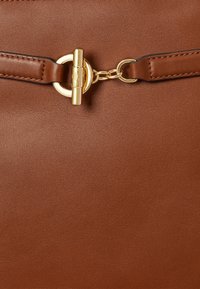 Barna bőrtáska aranyszínű fém zárakkal és lánc részletekkel, amelyek összekötik a két varrott bőrszíjat.