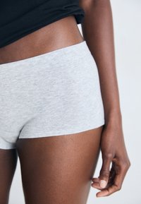 Woman wearing light gray fitted shorts and a black cropped top, showing midsection, thigh, and hand against plain background.