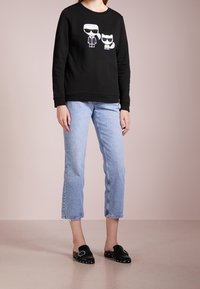 Sudadera negra con figuras de dibujos animados en blanco; combinada con jeans cortos de color azul claro y mocasines negros con acentos plateados. Textura suave.