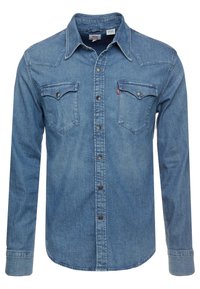 Ljusblå denimskjorta med lång ärm, tryckknappar, två bröstfickor, spetsig krage och kontrasterande sömmar. Slät textur.