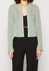 Ljusgrön, stickad cardigan med ett strukturerat, öppet stickmönster. Har en rundad halsringning och en kort design, med långa ärmar.