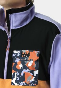 Fleecejack met een hoge kraag, een zwart lichaam, lila schouder en zoom, met een oranje en blauwe geprinte zak en ritsdetail.