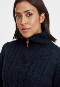 Navy knitted sweater with a high ribbed collar and zipper. Features cable knit patterns on the front and soft texture.