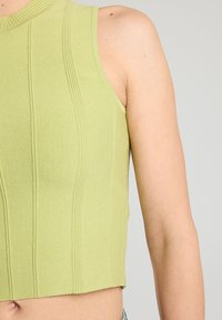 Top corto de punto en verde claro, con textura de canalé y diseño sin mangas. Presenta un escote alto y una silueta ajustada.