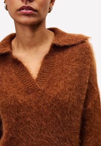 Brauner Strickpullover mit V-Ausschnitt und weitem Kragen, aus flauschigem Material gefertigt. Verfügt über Rippdetails am Kragen und Saum.