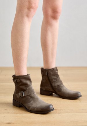 Braune Wildleder-Stiefeletten mit einer abgerundeten Zehe, seitlichen Reißverschlüssen und dekorativen Riemen. Niedrige Blockabsätze und eine weiche Textur runden das Design ab.