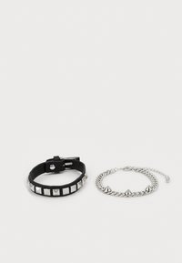 Bracelet en cuir noir avec des clous en pyramide argent�és et une boucle ajustable, à côté d'un bracelet en chaîne argenté avec trois pointes saillantes.