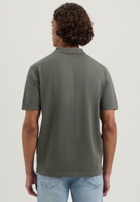 Mørkegrønn kortermet polo-skjorte med krage og glatt tekstur, parret med lyseblå jeans, som viser skjortens bakview.