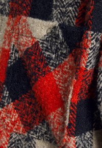 Tecido de lã com um padrão xadrez em vermelho, preto e cinza. Apresenta um acabamento texturizado e uma superfície suave e felpuda, com uma profundidade de fibra visível.