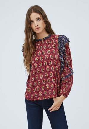 Blusa rossa a paisley con un bordo arricciato blu navy, maniche lunghe e una vestibilità comoda. Il tessuto ha una texture morbida e dettagli di pattern intricati.