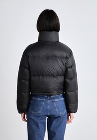 Svart dunjakke med høy krage, quiltet design og kort passform, paret med blå denimjeans. Synlige sømmer og lommer på jeansene.