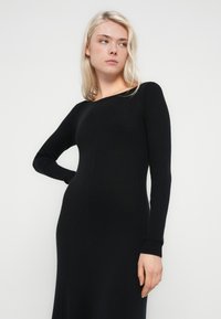 Black ribbed knit dress with long sleeves, fitted silhouette, and round neckline, featuring a smooth texture and elegant full-length design.