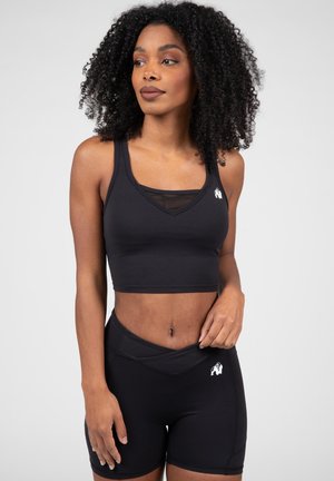 Zwarte sportieve crop top met een gaas-inzet en logo, gecombineerd met hoge zwarte shorts met een vergelijkbaar logo en een kruis ontwerp.