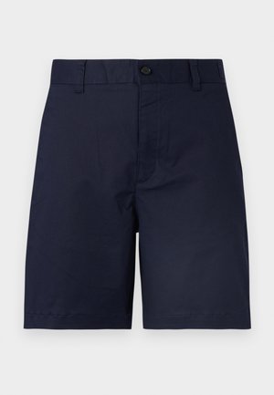 Tamsiai mėlyni šortai iki kelių su sagų užsegimu, diržo kilpelėmis ir lygiu priekiu, fone paprastas šviesus fonas.