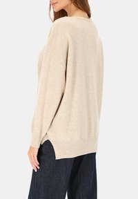 Beżowy sweter o luźnym kroju, z zaokrąglonym dekoltem, opuszczonymi ramionami i bocznymi rozcięciami. Wykonany z miękkiego, fakturowanego materiału. Dopasowany do ciemnych spodni dżinsowych.