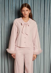 Ružový súbor na oddych pozostávajúci z košeľového vrchného dielu s golierom, zapínaného na gombíky a s mašľou, a širokých nohavíc, oba s textúrovanými pásikmi a tylovými ozdobami na manžetách.