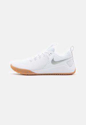 Chaussure de sport basse blanche avec semelle en gomme, tige en mesh, lacets et logo Nike Swoosh gris sur le côté.