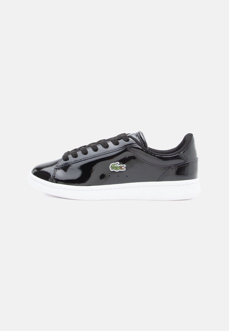 Baskets en cuir verni noir avec lacets noirs, semelle blanche et logo crocodile vert sur le côté, montrées en profil latéral sur fond blanc.
