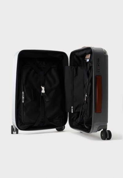 Valise rigide ouverte avec intérieur en tissu noir, compartiments zippés, sangles ajustables, quatre roues et une poignée latérale.