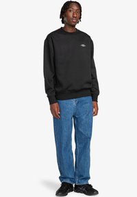 Felpa nera con scollo rotondo e un piccolo logo sul petto. Abbinata a jeans in denim azzurro chiaro e sneakers nere.