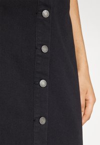 Hand resting beside a black garment with a row of silver snap buttons labeled "ONLY" down the side.