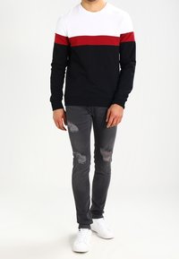 Camisa de hombre de manga larga con bloques de color blanco, rojo y azul marino; combinada con vaqueros grises desgastados y zapatillas blancas.