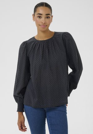 Black blouse with textured polka dot pattern, round neckline, and long puff sleeves with elastic cuffs, paired with blue jeans.