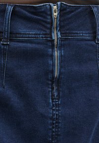 Tamsios mėlynos spalvos džinsai iš tamsaus džinso audinio su priekiniais užtrauktuko užsegimais, elegantišku aukštu liemeniu ir subtiliomis siuvimo detalėmis. Audinys yra lygios tekstūros su minimaliu blizgesiu.