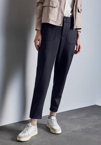 Pantalons en tissu doux et noir avec une coupe décontractée, dotés de grandes poches avant et d'une taille lisse. Portés avec des baskets aux teintes neutres.