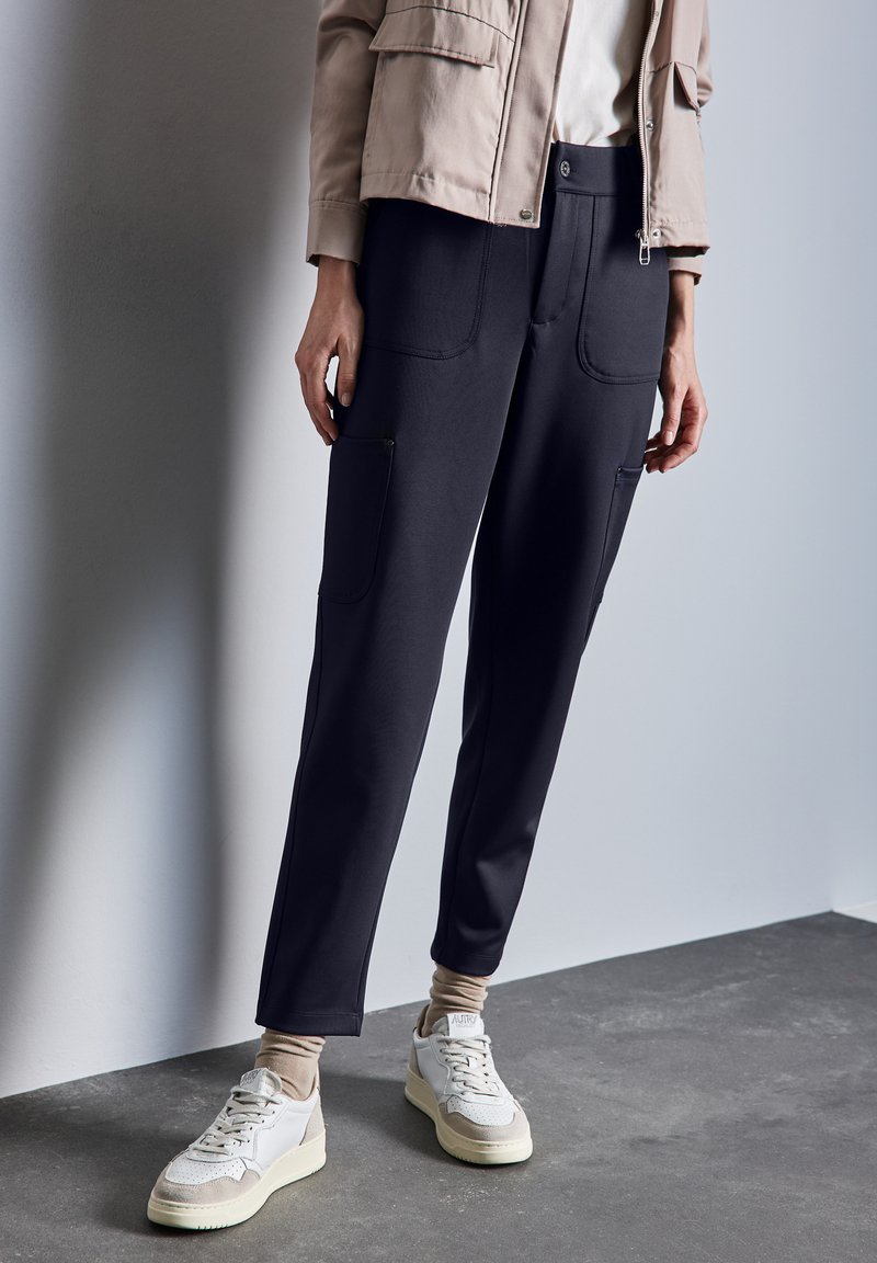 Pantalons en tissu doux et noir avec une coupe décontractée, dotés de grandes poches avant et d'une taille lisse. Portés avec des baskets aux teintes neutres.