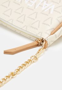 Valentino beige läderpouch med återkommande logomönster, guldfärgad hårdvara, dragkedjestängning och avtagbar kedjestrapsrem. Texturerad yta.