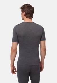 Hombre visto de espaldas con una camisa de manga corta gris oscuro ajustada y pantalones a juego, contra un fondo claro y simple.