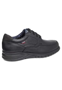 Zapato de cuero negro con punta redondeada, paneles laterales texturizados y suela acolchada. Presenta cordones y un pequeño detalle con logo.