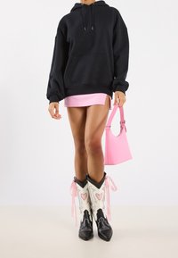 Černá oversize mikina s přední kapsou, sloučená s krátkou růžovou sukní, růžovou kabelkou a černobílými kovbojskými botami se srdíčkovými detaily.