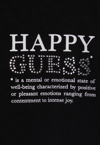 Tela negra con el texto impreso "HAPPY" en blanco y "GUESS" en brillantes strass plateados, acompañado de una definición abajo en texto blanco.