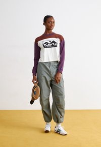 Långärmad croppad topp med vita och bruna sektioner som har en svart logotyp, i kombination med gröna cargobyxor och vita sneakers.