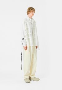 Camisa blanca de manga larga con tirantes en capas, puños abotonados; pantalones anchos de color crema; zapatos de tela ligeros de color gris claro.