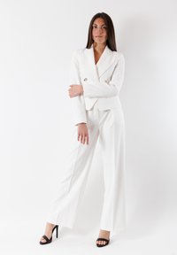 Completo bianco su misura con giacca doppiopetto e pantaloni a gamba larga. Tessuto liscio, design minimalista e dettagli con bottoni dorati.