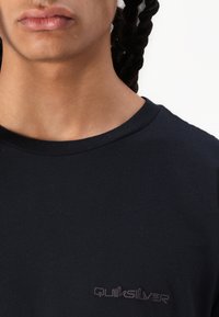 Fekete pamut póló, kerek nyakkivágással és rövid ujjakkal, az elülső bal oldalán diszkrét barna Quiksilver logóval.