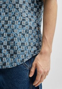 Korte mouwen shirt met een blauwe gebloemde stof met bladmotieven, zachte textuur en een afgeronde zoom, gecombineerd met donkerdenim jeans.