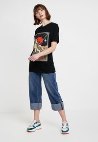 Sort grafisk t-shirt med et rumtema-design, parret med cropped blå denim jeans med opfoldede kanter og multikolore sneakers.