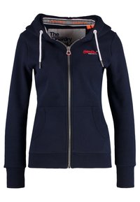 Felpa con zip di colore blu navy, con cappuccio foderato, lacci bianchi, due tasche frontali, polsini a coste e un logo sul petto. Materiale morbido.