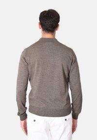 Maglione grigio a maglia con maniche lunghe e scollo rotondo, caratterizzato da una finitura testurizzata e polsini a costine, indossato con pantaloni bianchi.