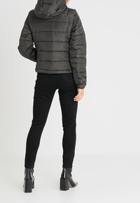 Sort dunjakke med horisontal syning og hætte, parret med sorte skinny jeans og ankelstøvler i patentlæder med chunky hæle.